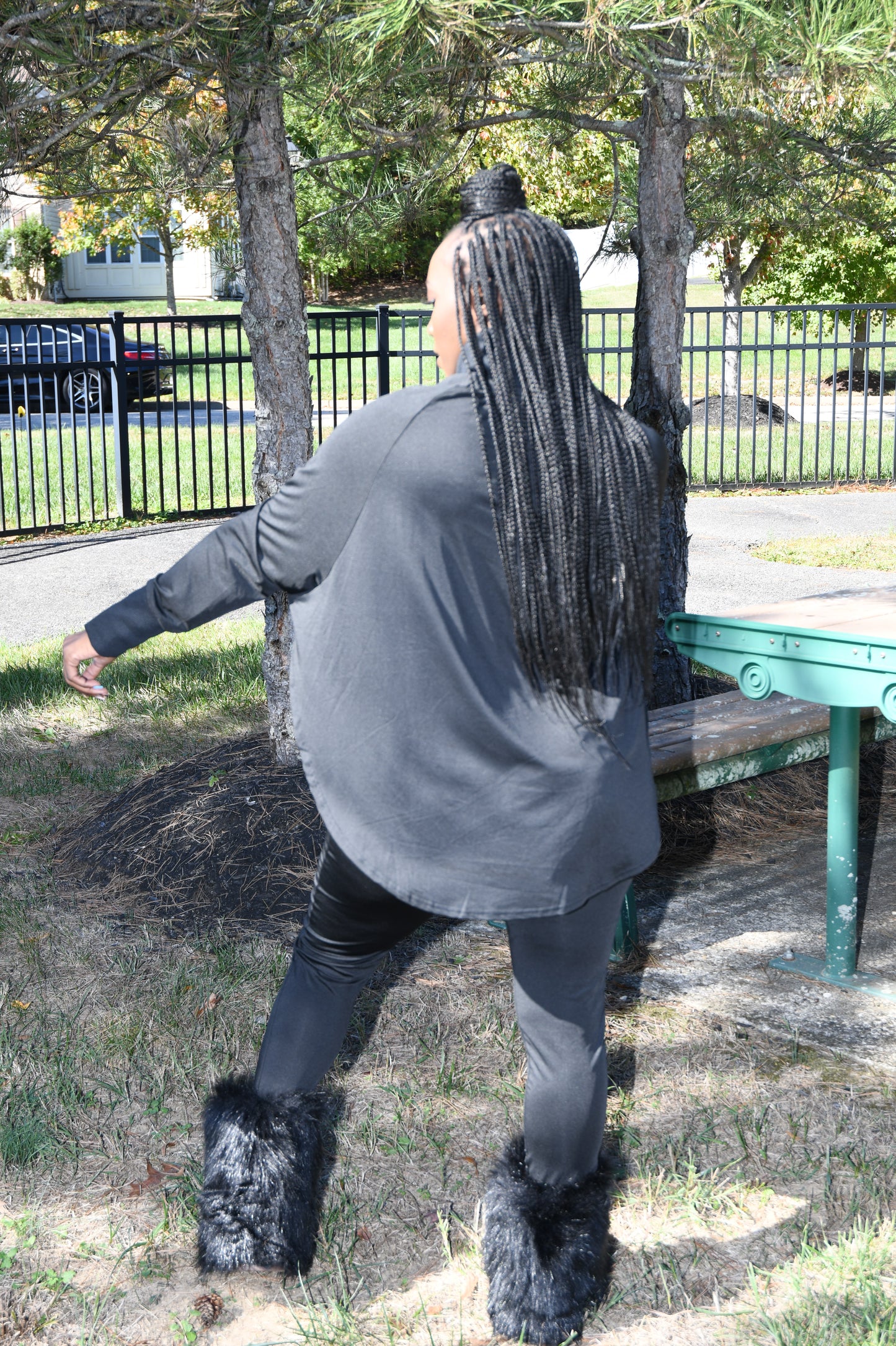 Person wearing a black sweatshirt and black boots standing on a tree branch with a park-like background.