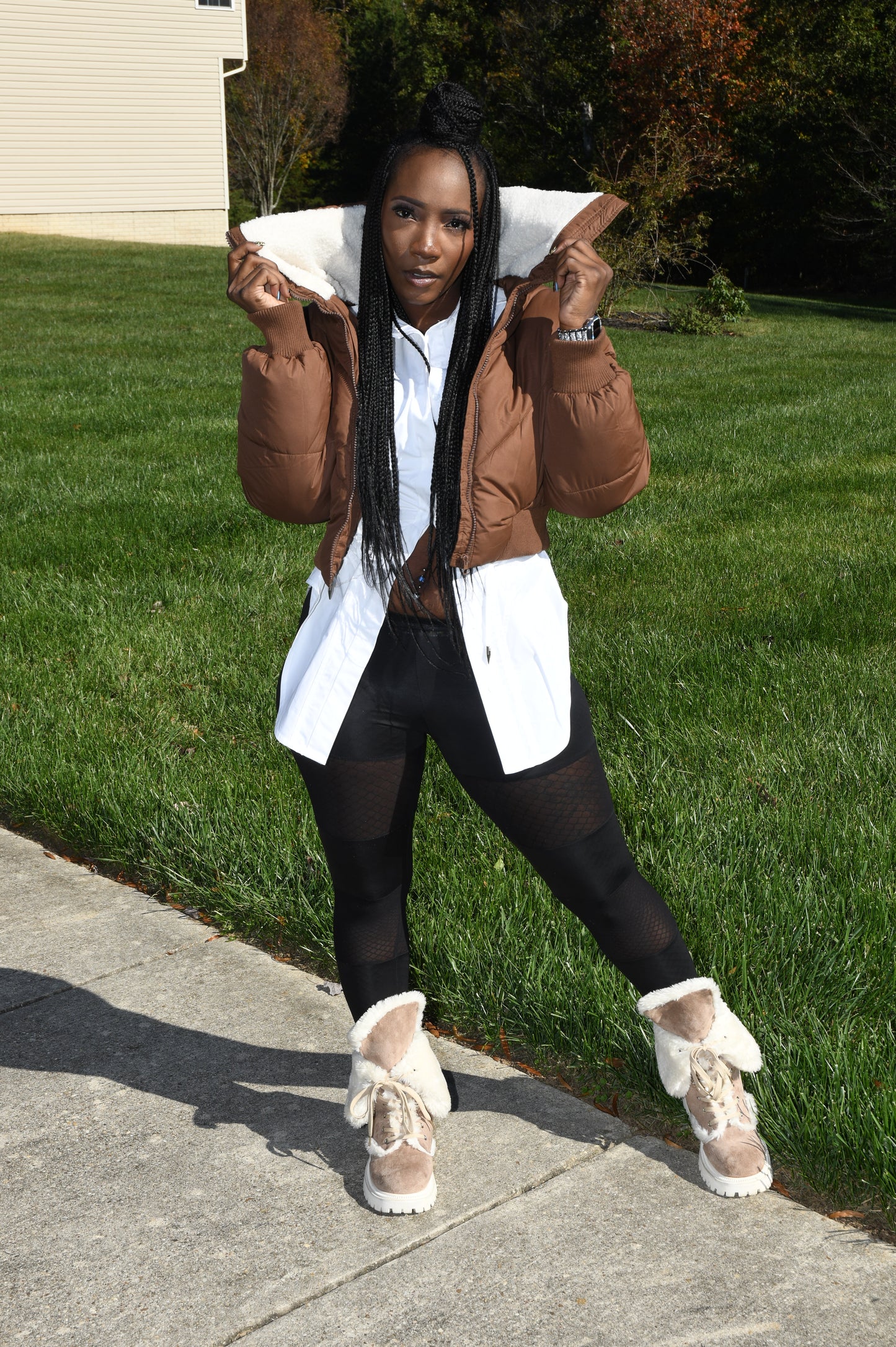 Person lying on grass wearing a brown coat and white shoes