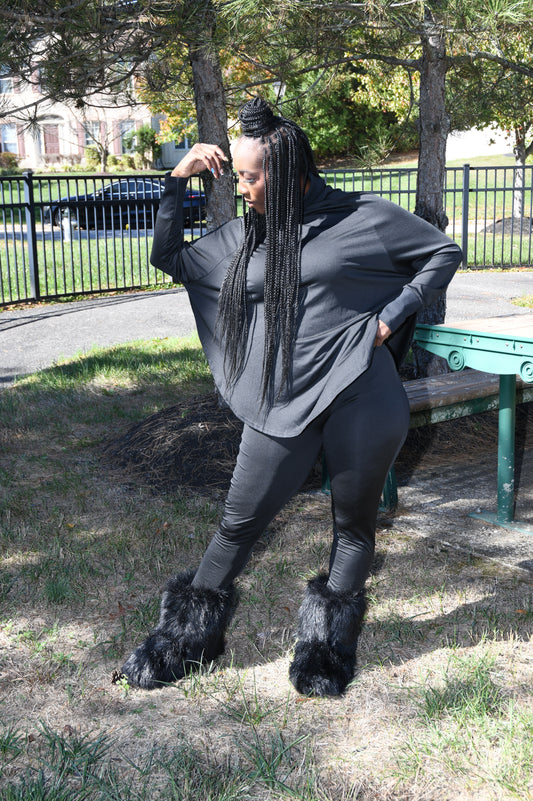 Person sitting on a bench in a park wearing a gray outfit with fur-lined shoes.