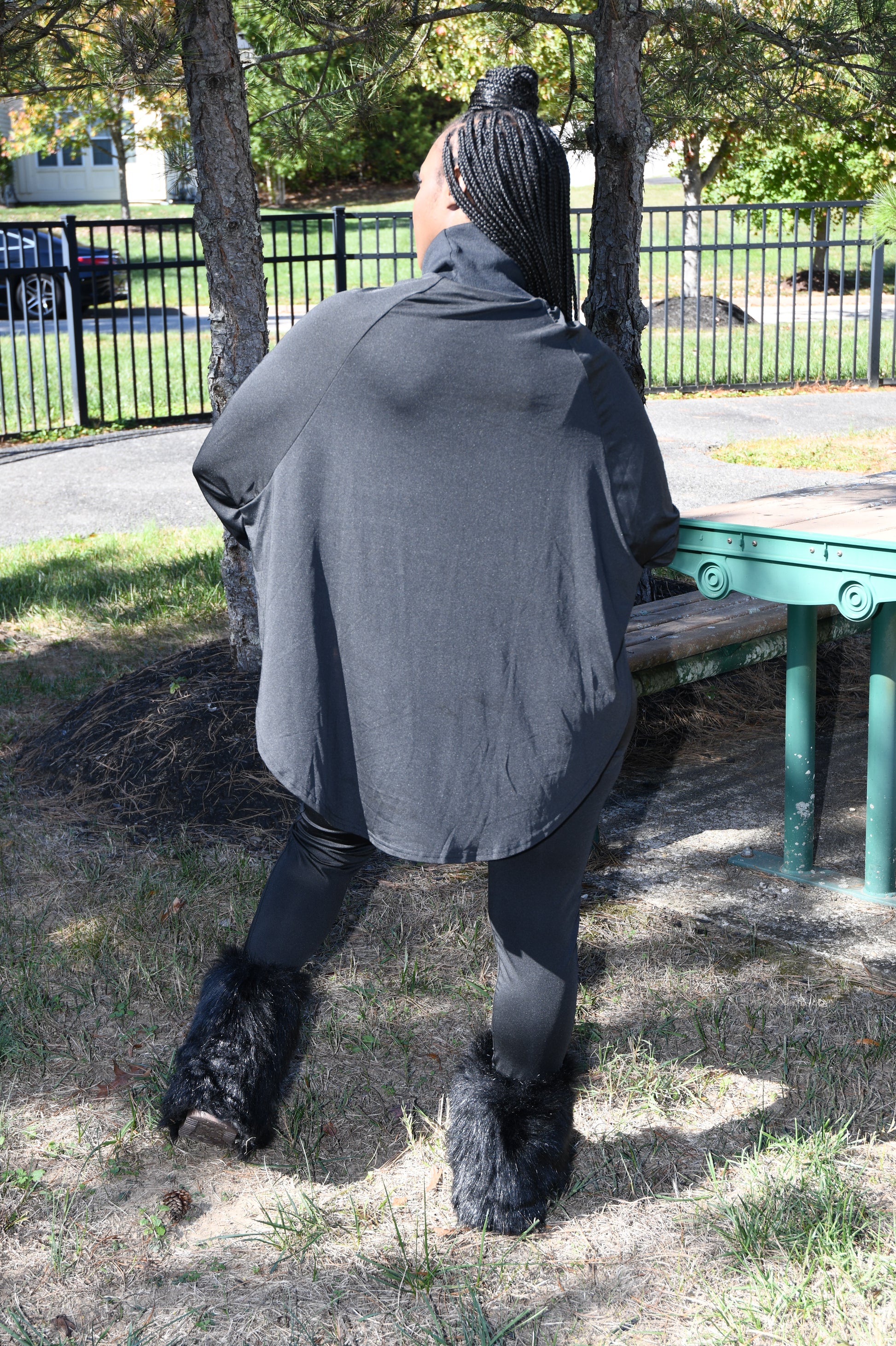 Person wearing a black cape set standing on a path with trees and a bench in the background. 