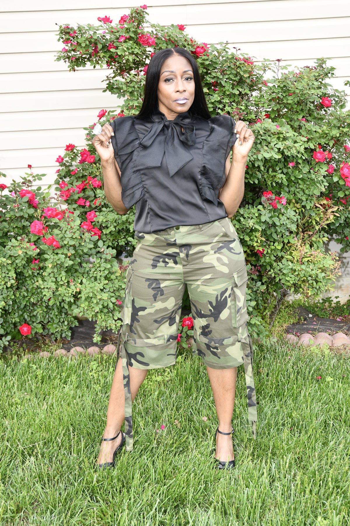 Person wearing camouflage pants and a black top standing in front of flowers and grass.