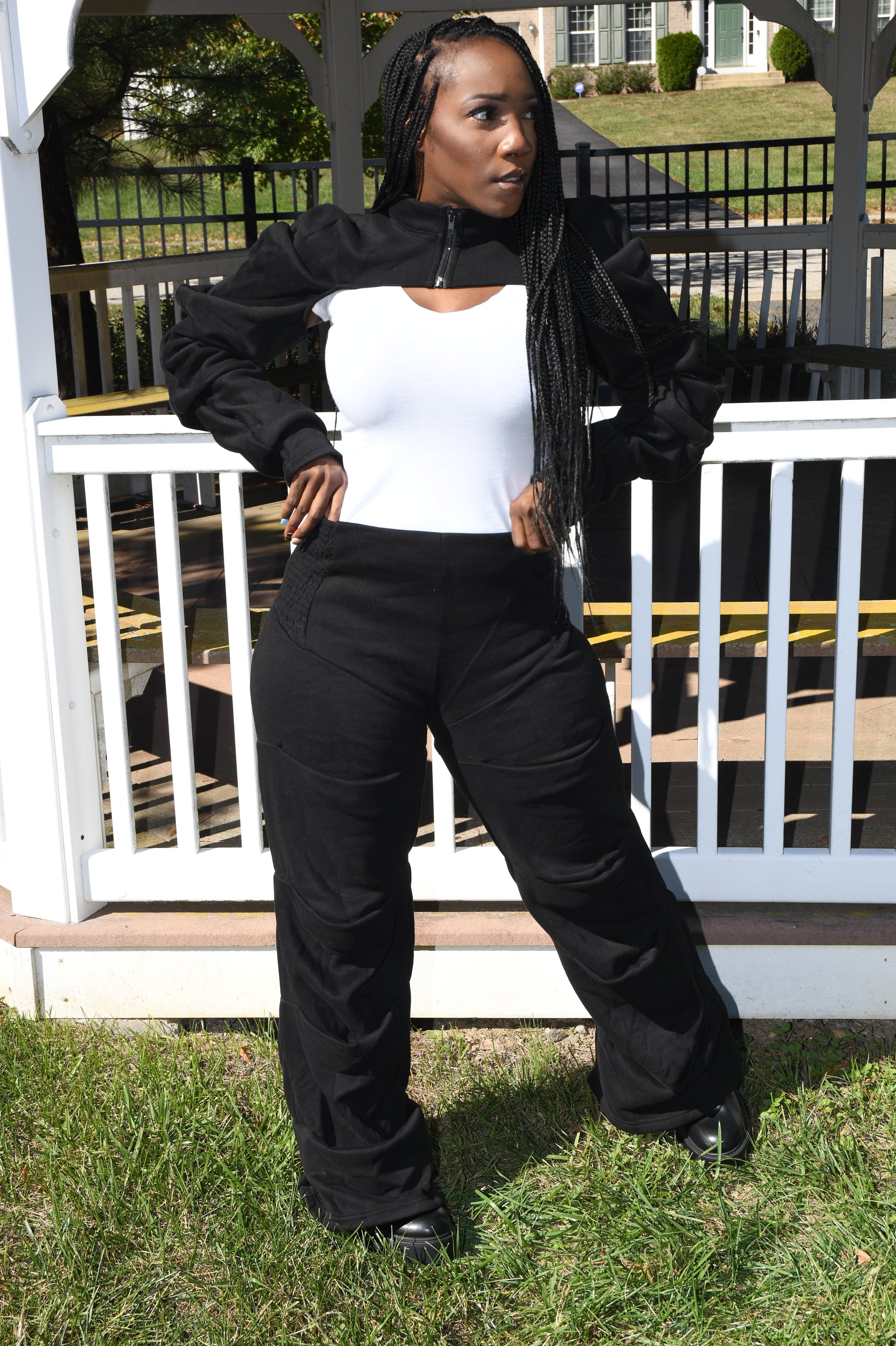 Person in black outfit with white shirt on grass and white fence background