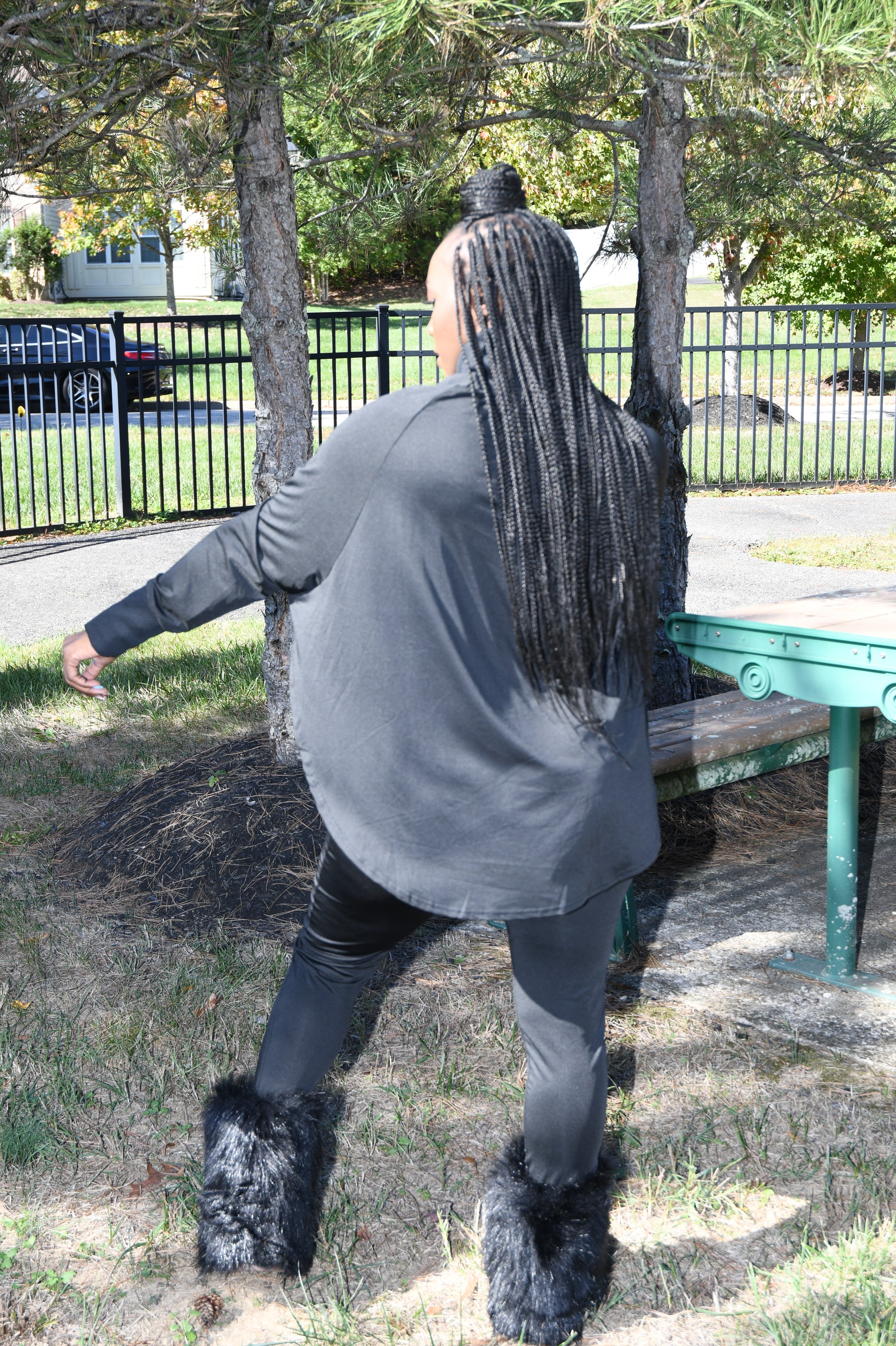 Person wearing a black sweatshirt and black boots standing on a tree branch with a park-like background.