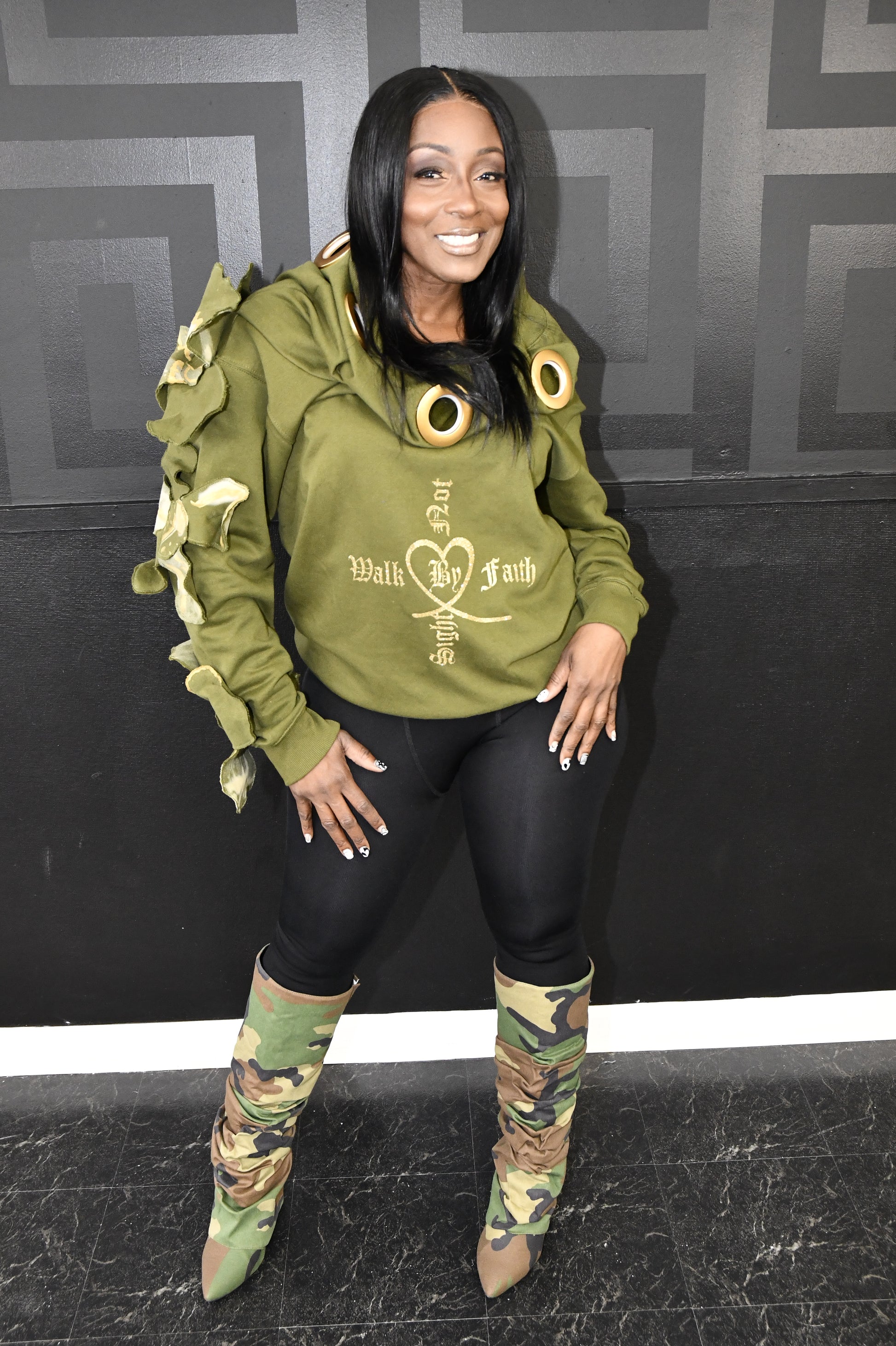 Person wearing a green hoodie with text and camouflage pants on a black and gray geometric patterned floor.